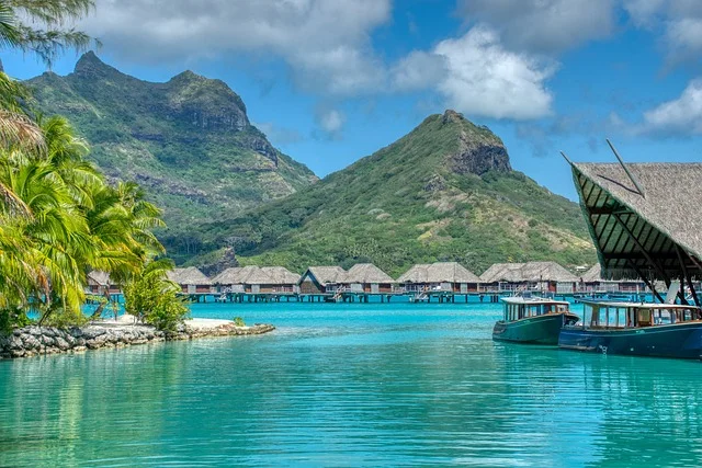 Lush mountains and cascading waterfalls in Tahiti, one of the most beautiful islands, with a black sand beach in the foreground.